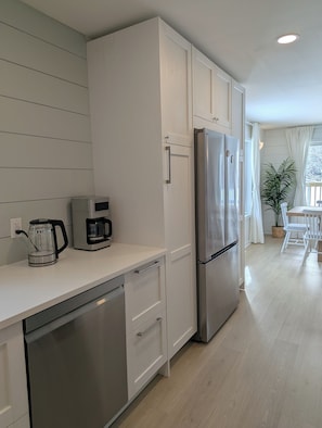 A modern kitchen with white cabinetry, stainless steel appliances, and a wooden floor.