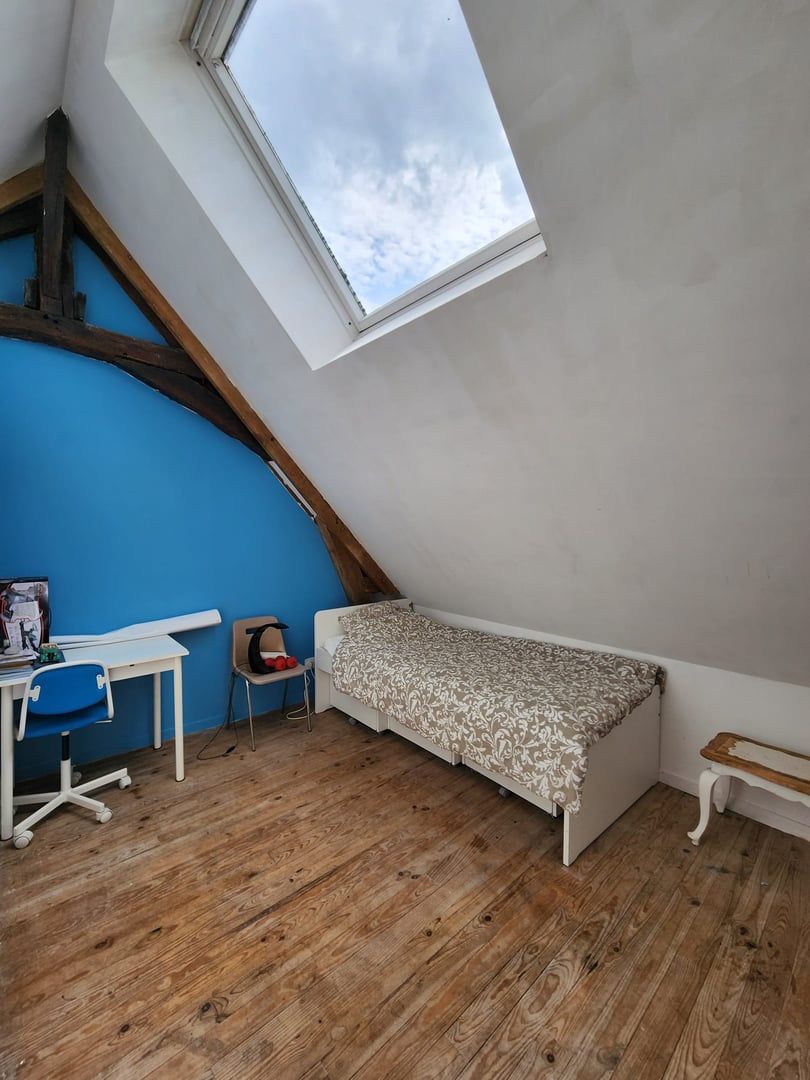 A small, sloped room with a skylight, a desk, a chair, and a bed.