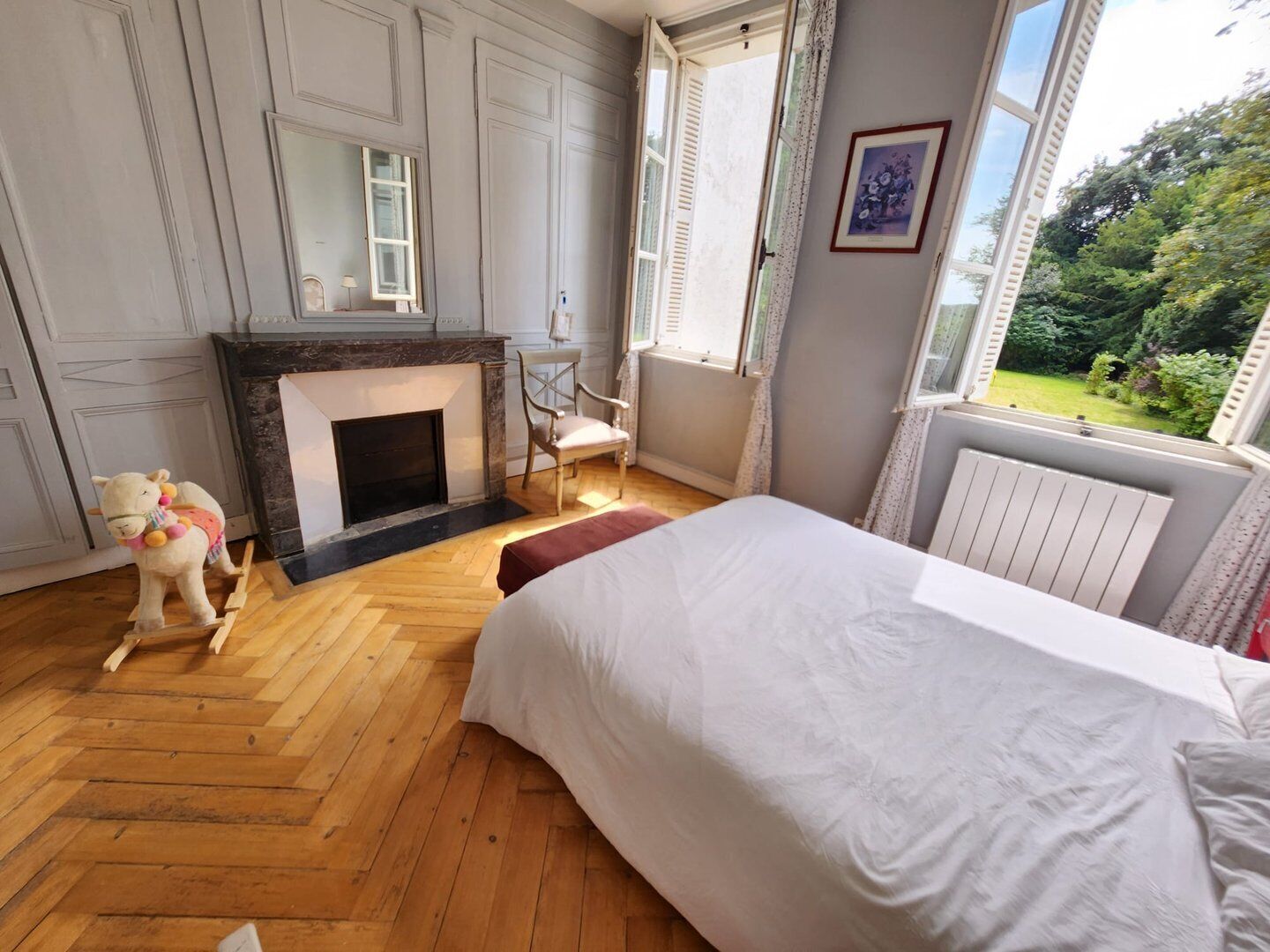 Une chambre avec une cheminée, un lit, une chaise et une fenêtre donnant sur un paysage verdoyant.