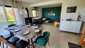 Un coin repas avec une table en bois dressée pour six personnes, entourée de chaises. On aperçoit un canapé et un meuble en arrière-plan.