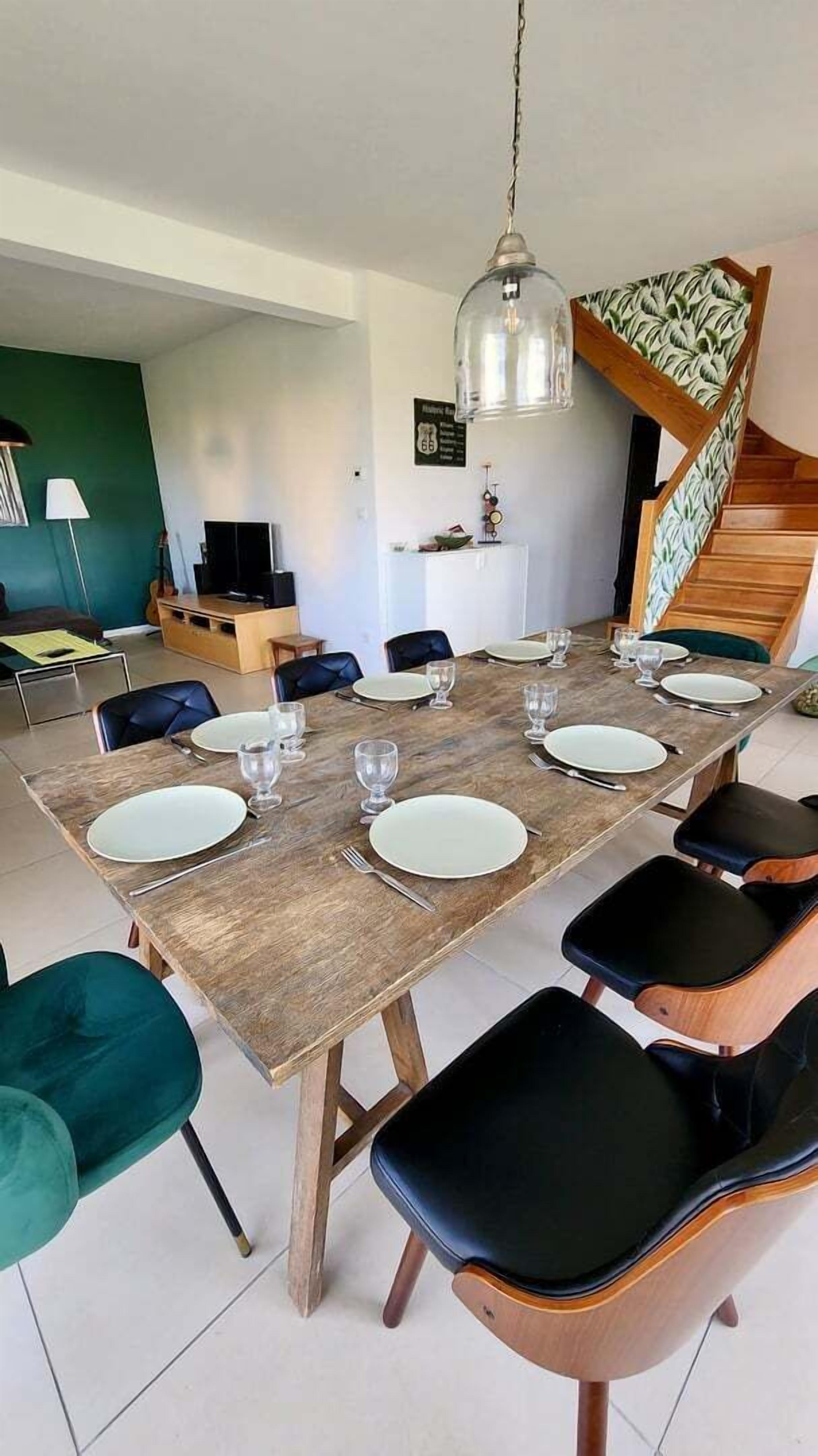 Ein Essbereich mit einem Holztisch, gedeckt für sechs Personen, umgeben von schwarzen und türkis-farbenen Stühlen.