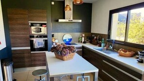 Une cuisine moderne dotée d’un îlot central, de deux tabourets, d’un four à micro-ondes, d’un four et de luminaires suspendus.