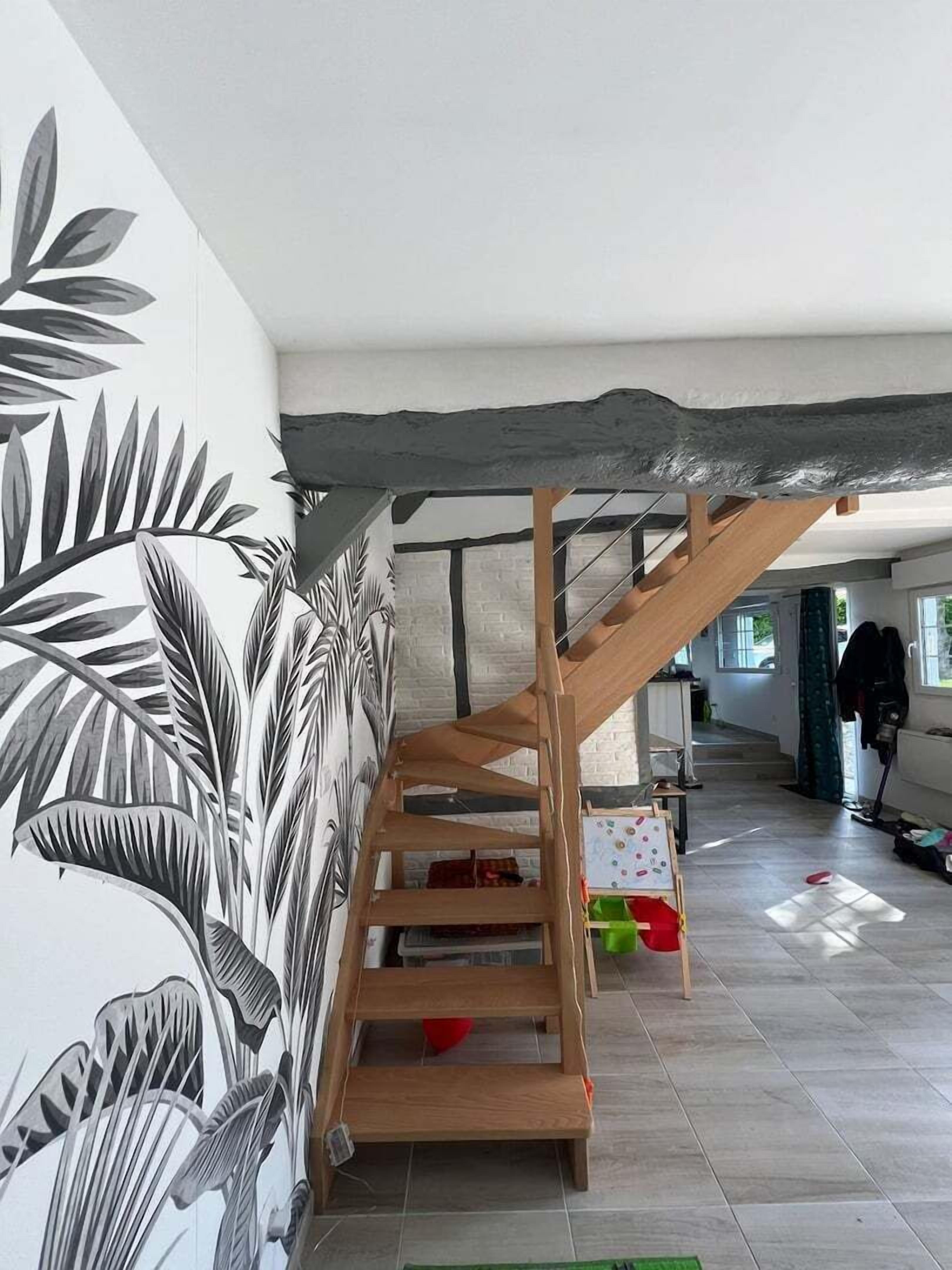 Eine Treppe mit Holzgeländer und Stufen, die zu einem Landeplatz mit weißer Wand und einer großen schwarz-weiß Blattform-Mural führt.
