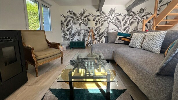 A living room with a glass coffee table, a sofa, a chair, a fireplace, and a wall with a tropical leaf pattern. - Old-fashioned charm with modern comforts (Doudeville)