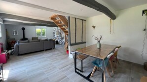 A spacious living area with a wooden dining table, a sofa, and a staircase leading to another level. - Old-fashioned charm with modern comforts (Doudeville)