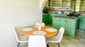 Zona pranzo con un tavolo rotondo e sedie bianche, cucina con mobili verdi e pavimento piastrellato.