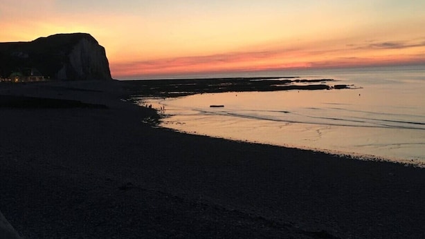 Uma praia com falésias e águas calmas durante o pôr do sol.