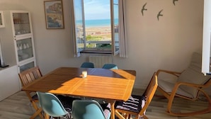 Quarto com mesa de madeira, cadeiras, vista para a praia, radiador e um armário com portas de vidro.