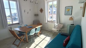 Uma sala de estar luminosa com uma mesa de jantar de madeira e cadeiras, um sofá verde-água e uma mesa redonda branca.
