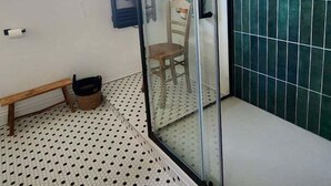 Et badeværelse med glasvæg omkring bruseren, flisegulv og et siddebænk.