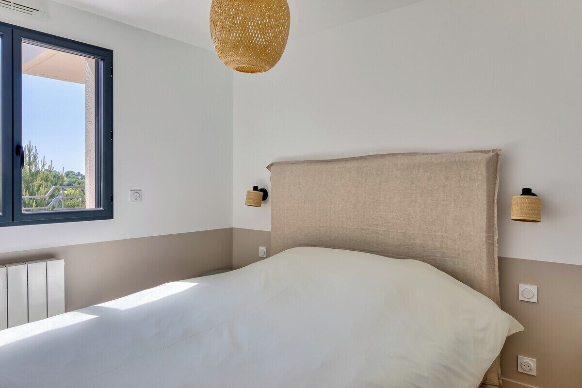 A bedroom with a bed, a window, a wall-mounted lamp, and a ceiling light.