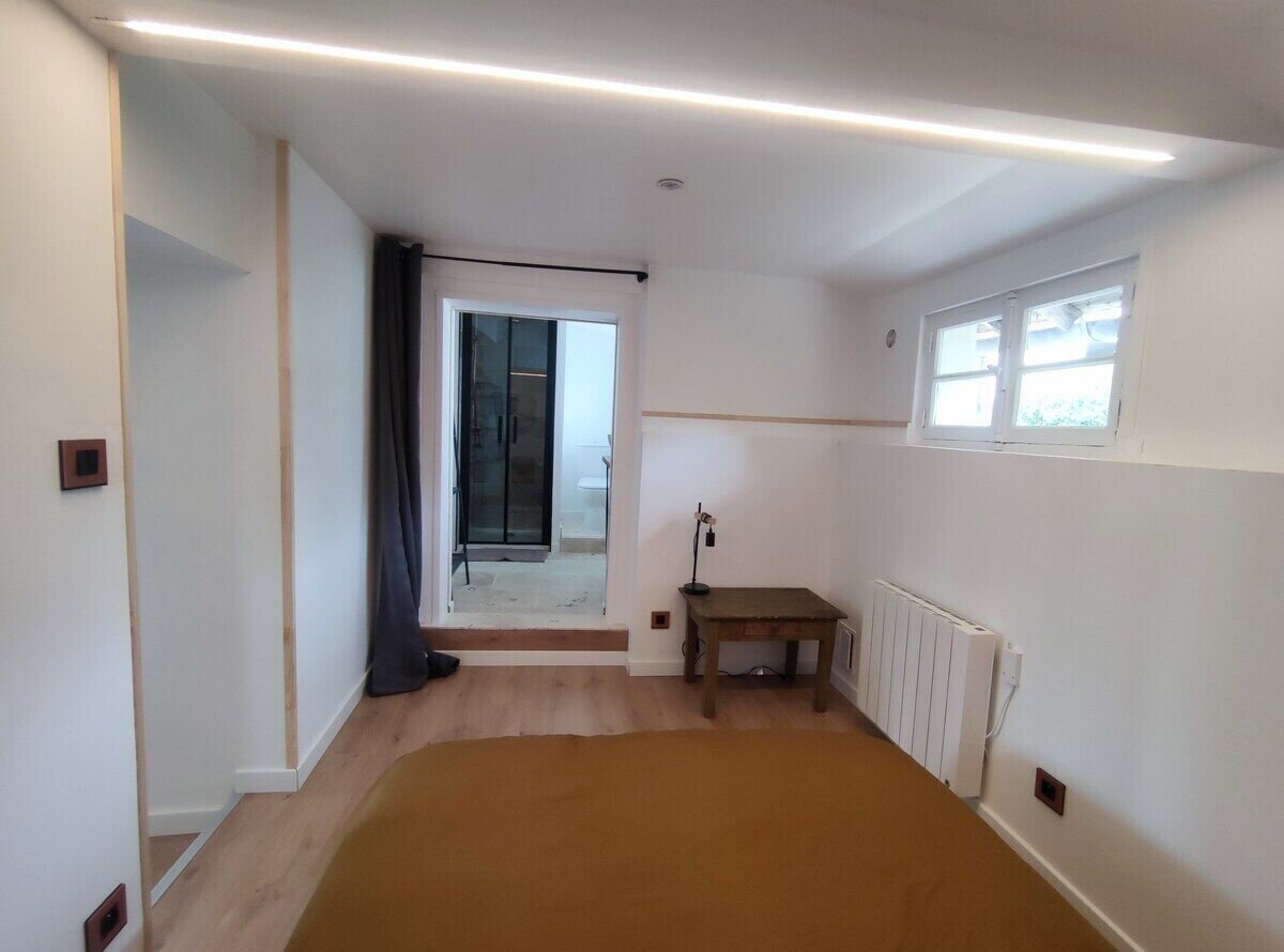 Une chambre avec un grand lit, une petite table, un radiateur et une fenêtre.