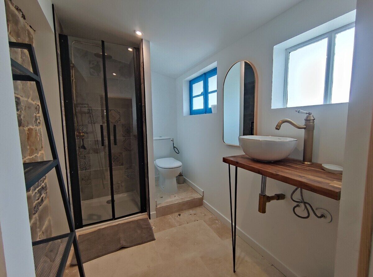 A bathroom with a glass shower enclosure, a white sink with a vessel basin, and a large mirror above the sink.