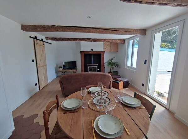 Un coin repas avec une table ronde en bois, dressée pour quatre personnes, entourée de chaises. Un téléviseur est fixé au mur au fond de la pièce.