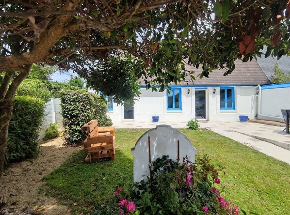 A white building with blue trim, a wooden bench, and a gravestone in the foreground.