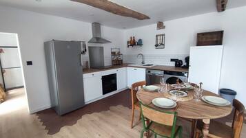 Een keuken met witte kasten, een grijze koelkast, een houten eettafel met stoelen en een hangende lamp.
