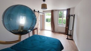 Ett sovrum med en stor säng, en hängande, sfärisk lampa, ett fönster med gardiner och ett element.