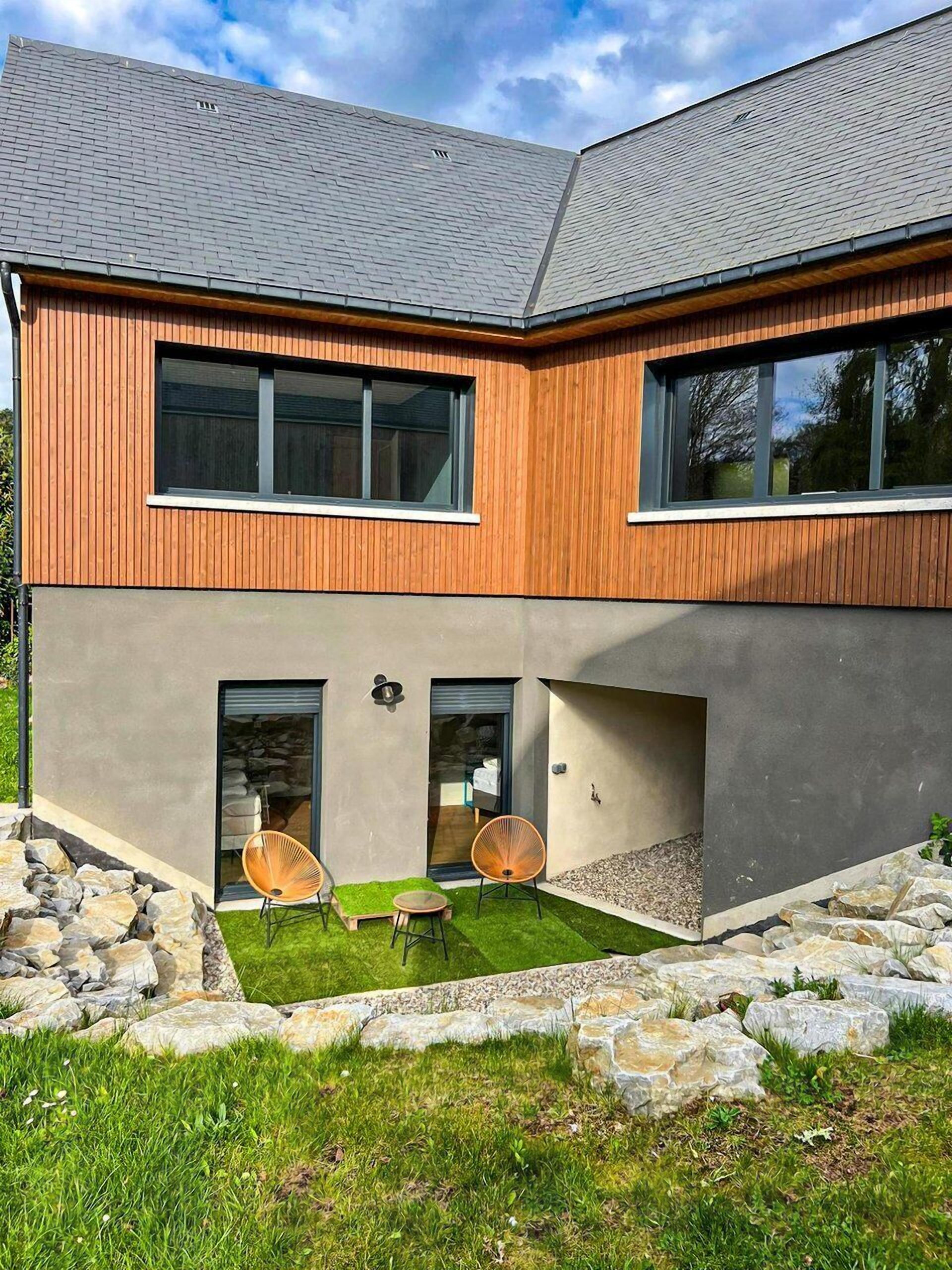 Une maison moderne à deux étages, dotée d’une façade en pierre, de grandes fenêtres et d’un chemin en pierre menant à l’entrée.