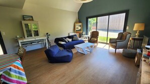Ein geräumiges Wohnzimmer mit großem Fenster, einem blauen Sofa, einem weißen Couchtisch und einem gestreiften Bett.