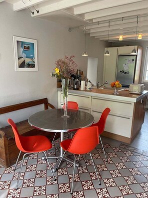 Zona pranzo con tavolo rotondo e sedie rosse, cucina con frigorifero e lavello, e piastrelle decorative al pavimento.