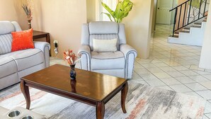 Una sala de estar con un sofá, un sillón, una mesa de centro y una escalera que lleva a otra habitación.