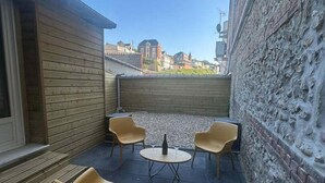 A small outdoor seating area with a table and chairs, a stone wall, and a view of buildings in the background. - Wooden duplex and sea in Fécamp, sea 50 m away (Fécamp)
