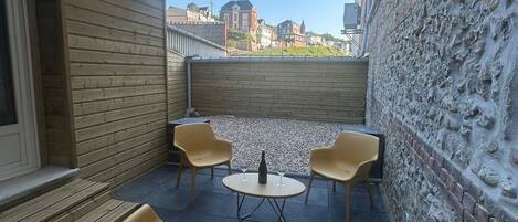 A small outdoor seating area with a table and chairs, a stone wall, and a view of buildings in the background.