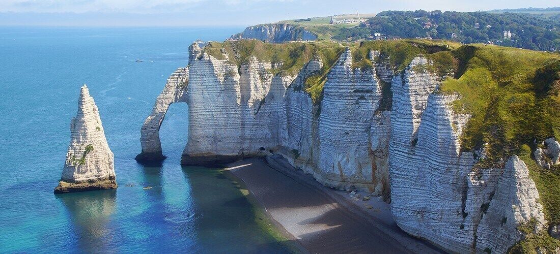 Une falaise côtière avec des formations de calcaire blanc et une étroite plage.