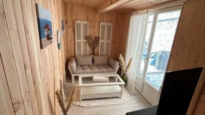 A cozy cabin interior with wooden walls, a sofa, a coffee table, a TV, and a window with a view. - Wooden duplex and sea in Fécamp, sea 50 m away (Fécamp)