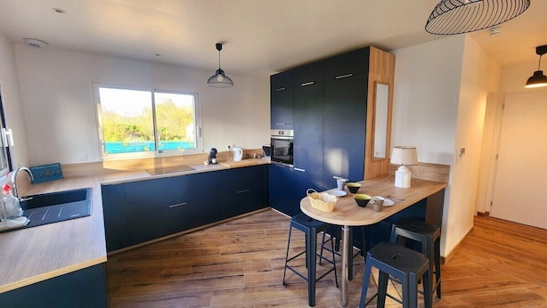 A modern kitchen with dark blue cabinets, a wooden countertop, and a bar area with stools. - The countryside at the edge of the sea (Manneville-ès-Plains)