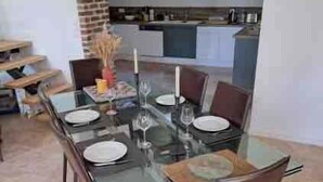 A dining area with a glass table, chairs, and a brick wall. - L'Écho de la Nature | Norman Farm • 1ha • Near Veules & Étretat (Sasseville)