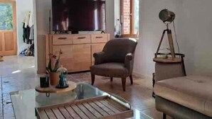 A living room with a glass coffee table, a sofa, a television on a wooden cabinet, and a tripod. - L'Écho de la Nature | Norman Farm • 1ha • Near Veules & Étretat (Sasseville)