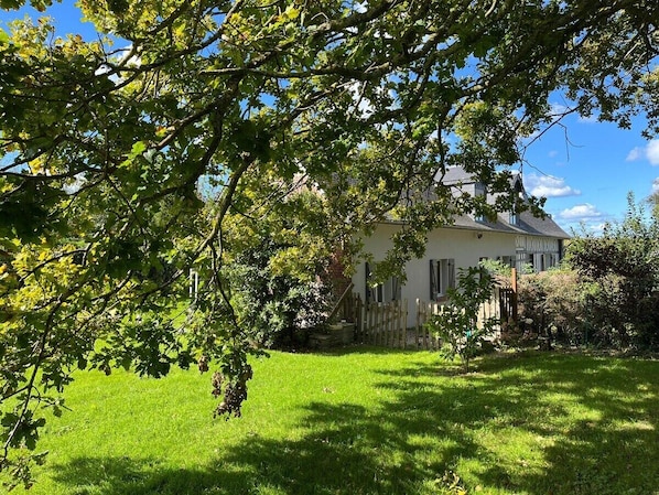 Une maison à l’extérieur blanc, entourée d’une pelouse bien entretenue et d’arbres.