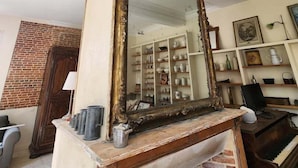 A room with a large mirror on a wooden stand, a brick fireplace, and a piano.