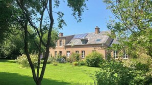 A large brick building with a sloped roof, surrounded by a well-maintained lawn and various trees.