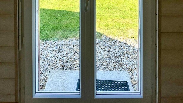Eine Glastür führt in einen Garten mit einem Holler Shed, einem Rasen und einem Kiesplatz.