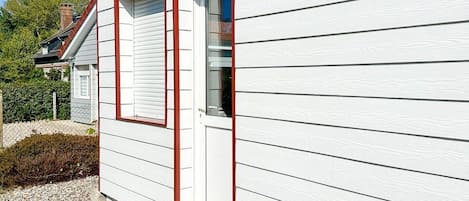 A white building with horizontal siding, a red door, and a small porch with steps.