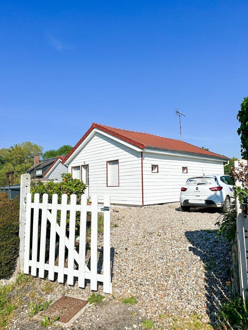 A white single-story house with a red roof, a white picket fence, and a parked car in front.
