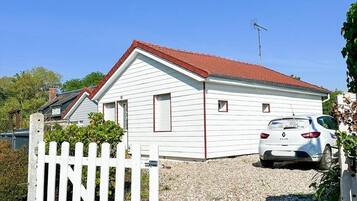 A white single-story house with a red roof, a white picket fence, and a parked car in front.