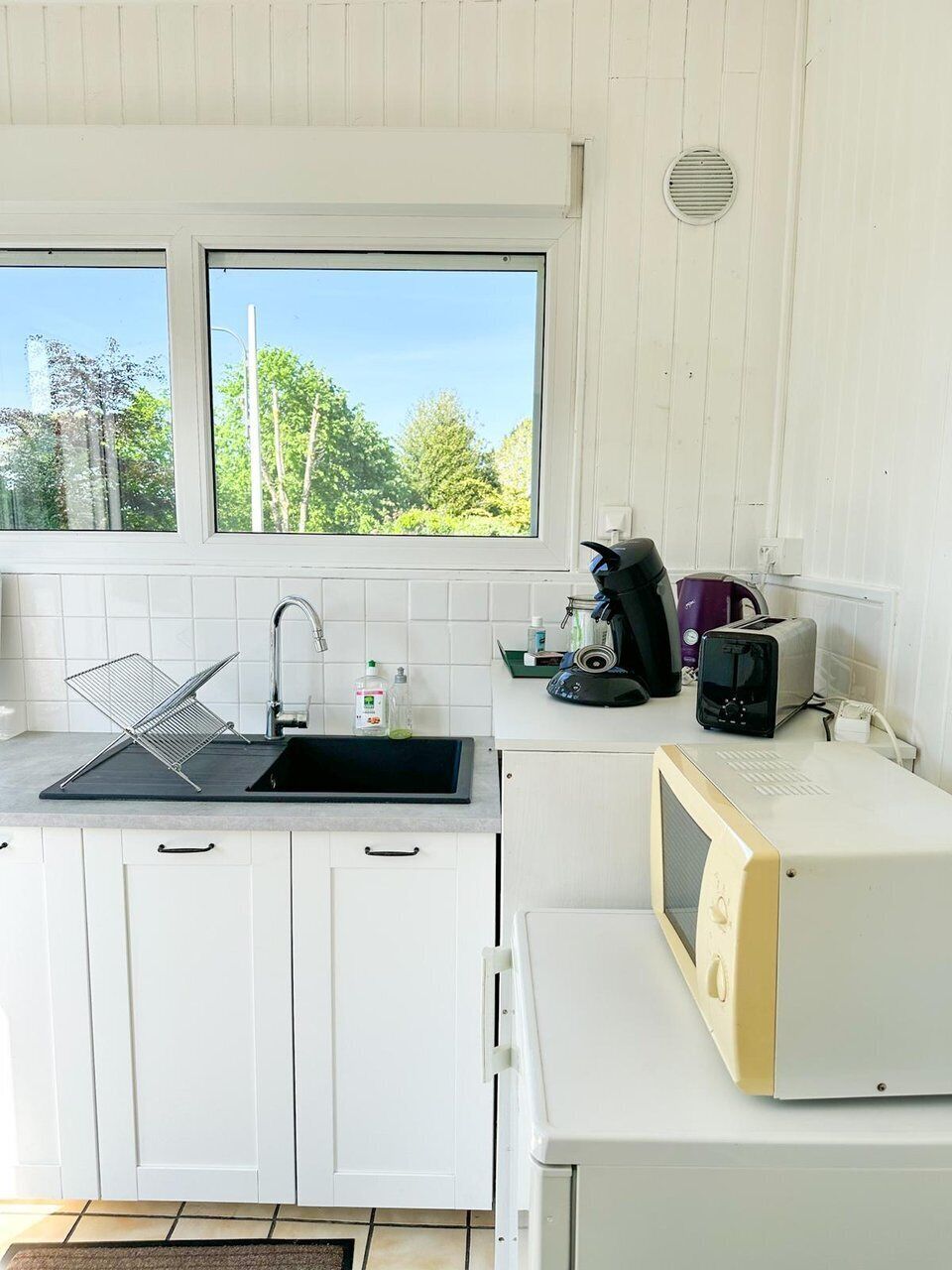Una cocina con ventana, armarios blancos, microondas, tostadora y cafetera.