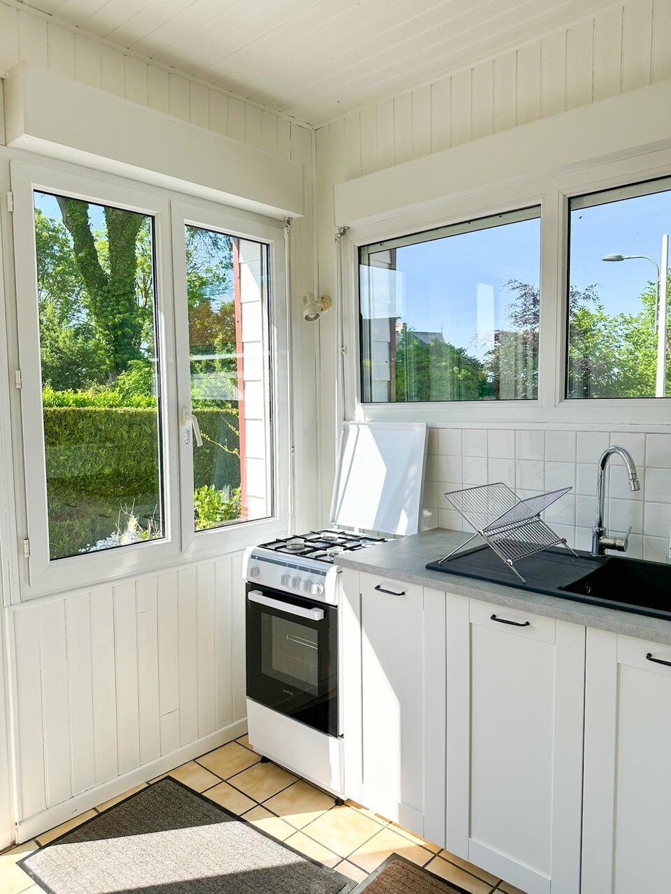 A kitchen with white cabinets, a stove, a sink, and large windows.