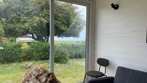 A room with a large sliding glass door leading to a garden. Inside, there is a grey sofa and a green chair. - Anchoring, cottage near the sea (Sotteville-sur-Mer)