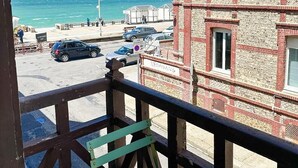 Un balcon donnant sur la mer, un immeuble à la façade en briques et des voitures garées dans la rue.