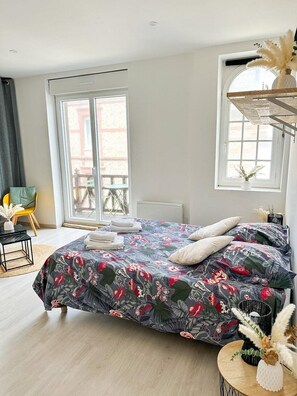 A bedroom with a bed, a window, a chair, and a small table.
