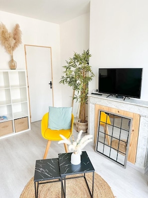 Ein Wohnzimmer mit Fernseher, einem gelben Sessel, einem kleinen Tisch, einem Bücherregal und einem Kamin.