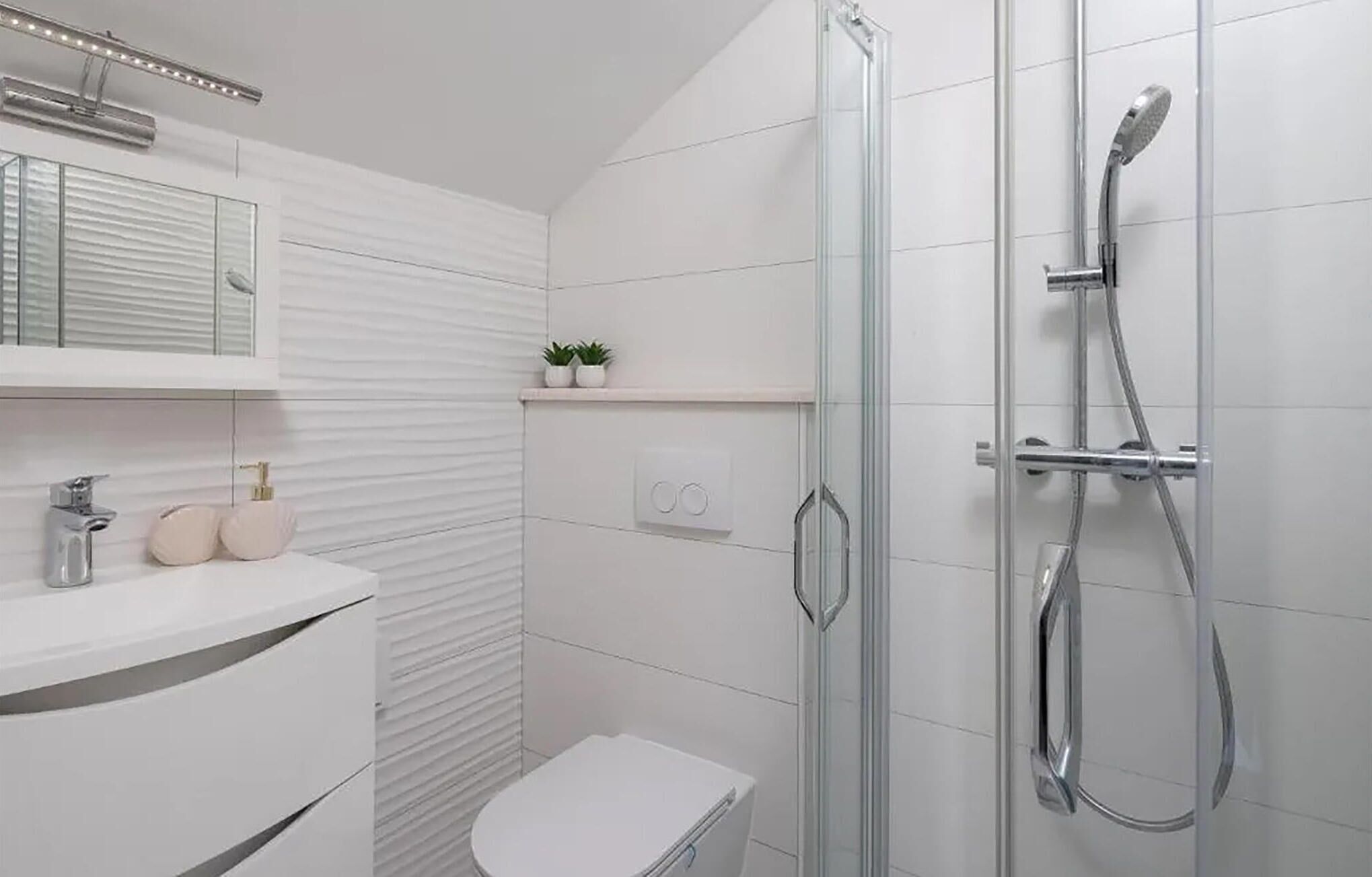 Een moderne badkamer met een douchecabine van glas, een wit toilet, een wastafel met spiegel en een klein plankje met planten.