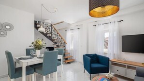 Ett modernt vardagsrum med en matplats, en trappa med ett blommigt mönster, en blå fåtölj och en platt-TV.