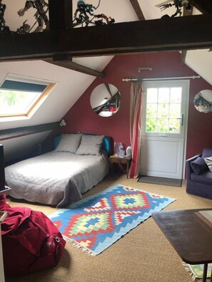 Un dormitorio acogedor en el ático, con cama, una mesita, un bolso rojo y una alfombra colorida.