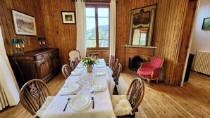 Ein Esszimmer mit einem langen Tisch für sechs Personen, Holzwandverkleidung, einem Kamin und Blick durch ein Fenster.