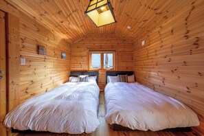 Une cabane avec deux lits, des murs en bois, une fenêtre et un luminaire au plafond.